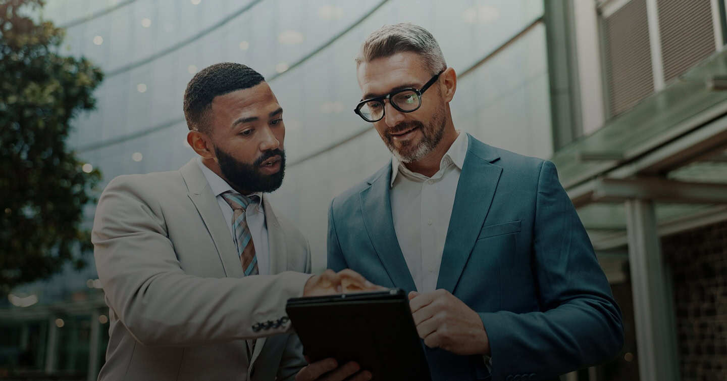 Two men wearing suits looking at a tablet together