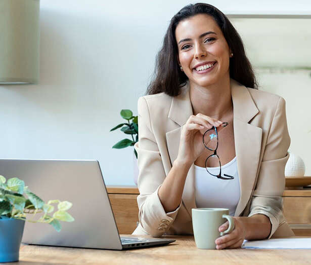 Woman holding her glasses and a coffee cup while sitting at a desk