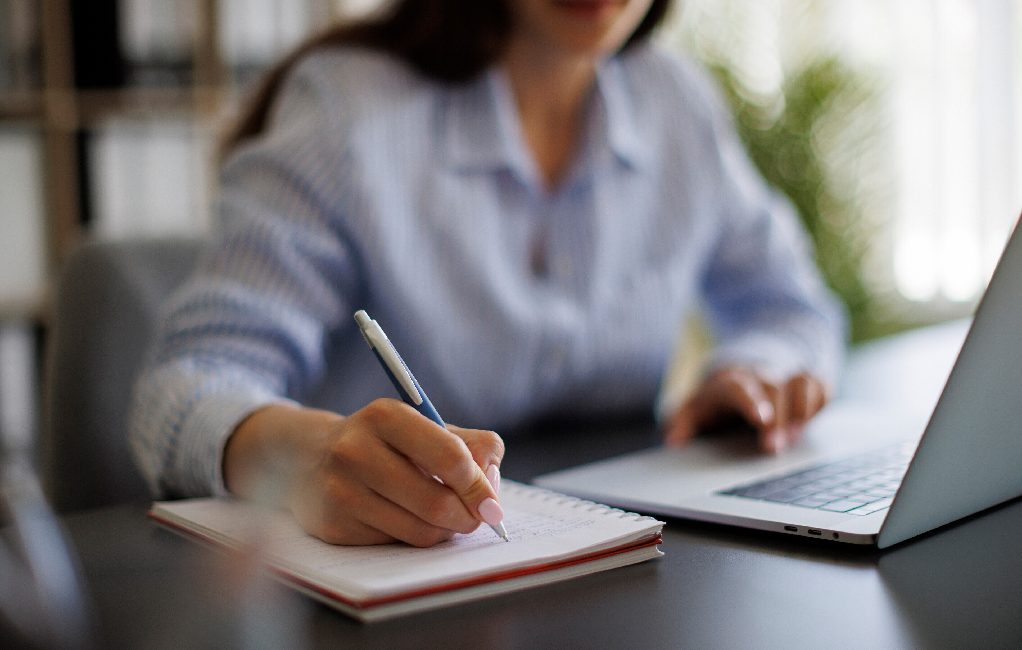 woman taking notes on pad from laptop